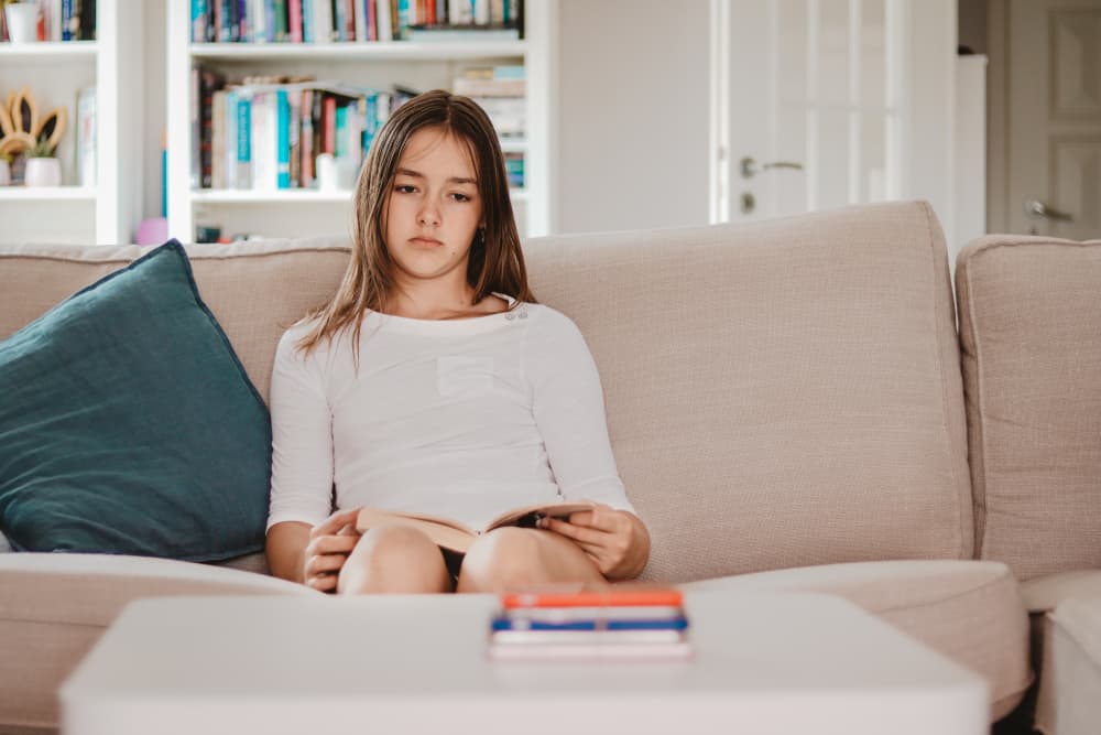 Ein Mädchen in einem weißen T-Shirt sitzt traurig mit einem Buch in den Händen auf der Couch