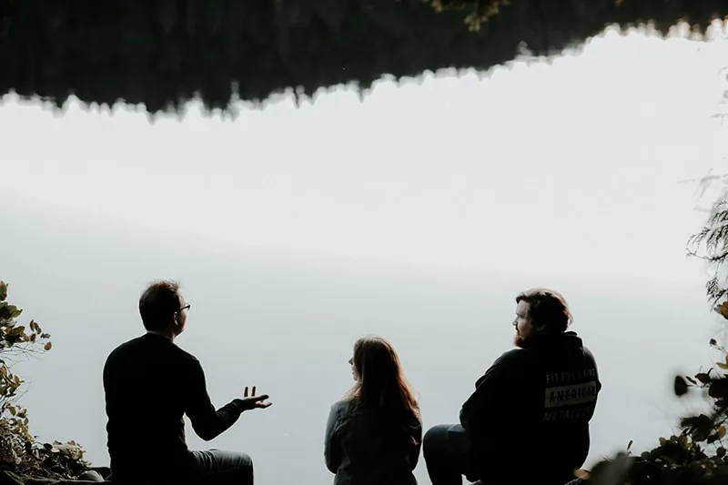 Ein Mann spricht mit Freunden, während er in der Nähe eines Gewässers sitzt