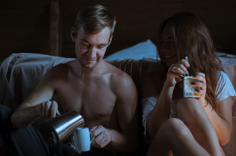 Ein Mann füllt die Tasse Kaffee neben einer Frau, die in einer intimen Atmosphäre Saft hält, während sie neben einem Bett sitzt