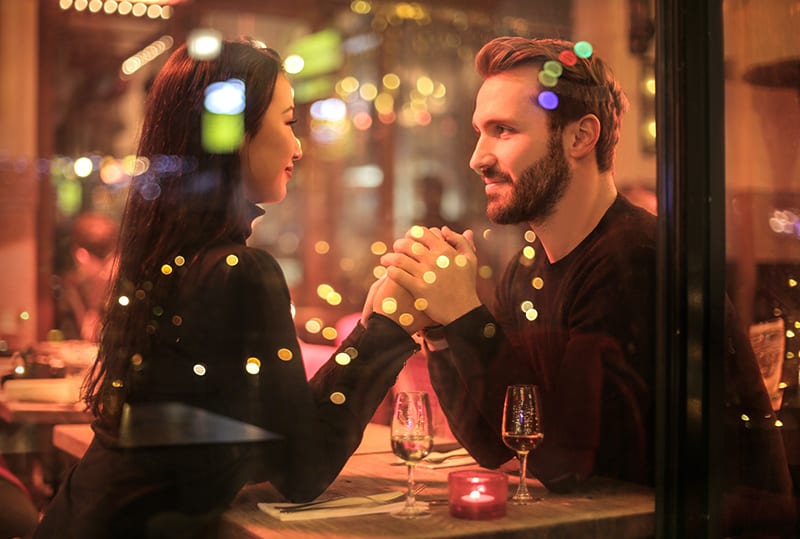 Ein Mann hält die Hand einer Frau, während er im Restaurant sitzt und Champagner trinkt