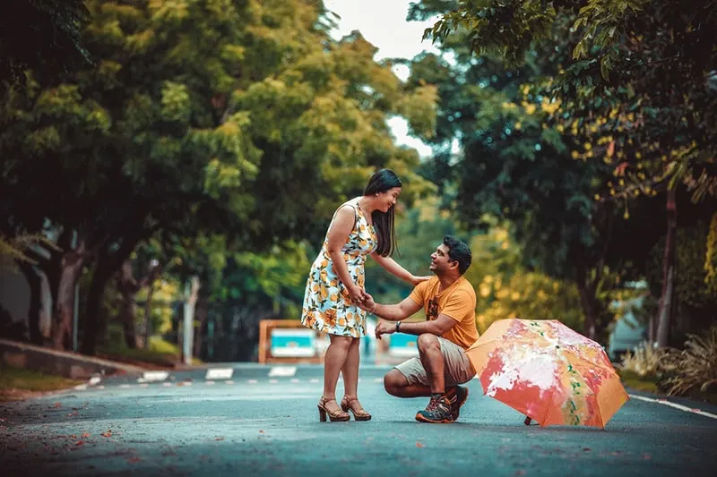 ein Mann kniet vor einer Frau neben einem Regenschirm auf der Straße