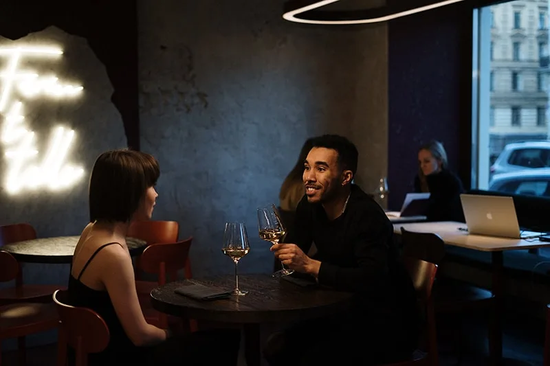 Ein Mann lehnte sich auf den Tisch und hielt ein Glas Wein vor eine Frau im Restaurant