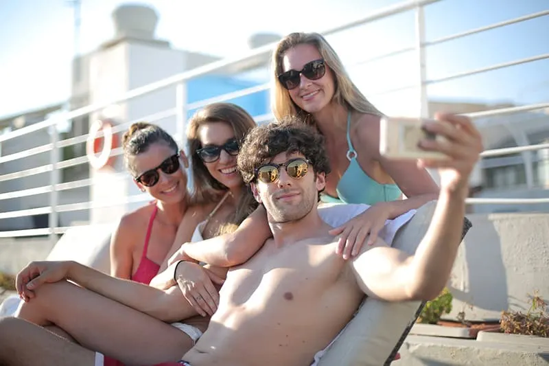 Ein Mann macht ein Selfie, umgeben von drei Freundinnen im Schwimmbad