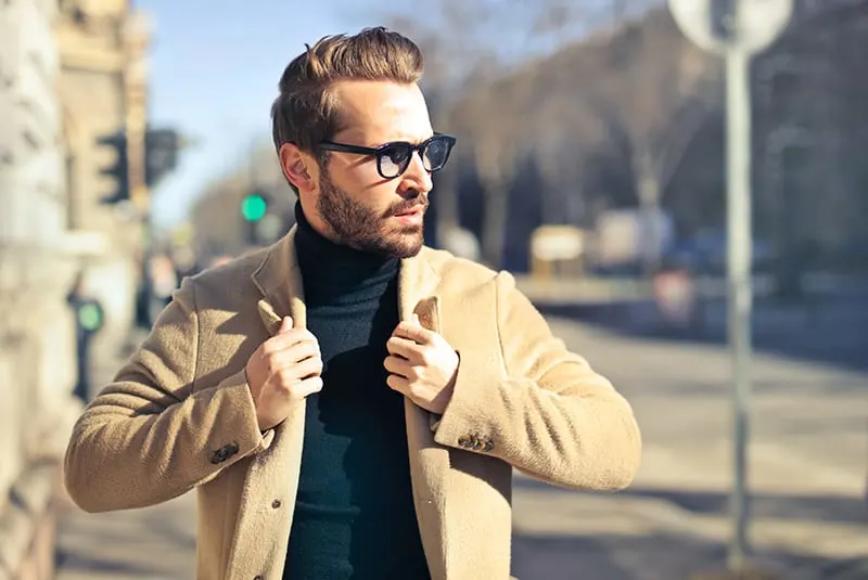 Ein Mann mit Brille und brauner Jacke geht auf dem Bürgersteig spazieren