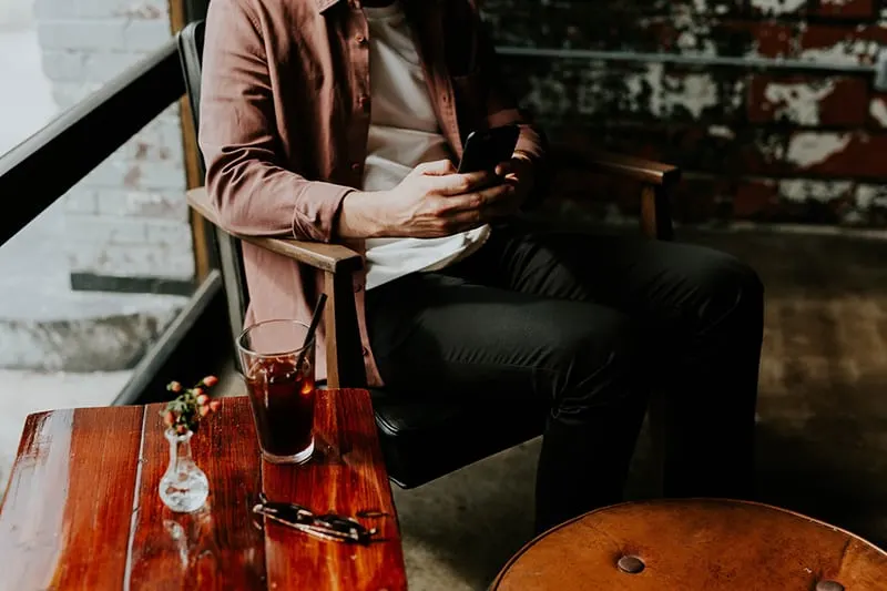 Ein Mann schreibt eine Nachricht auf das Smartphone, während er etwas trinkt