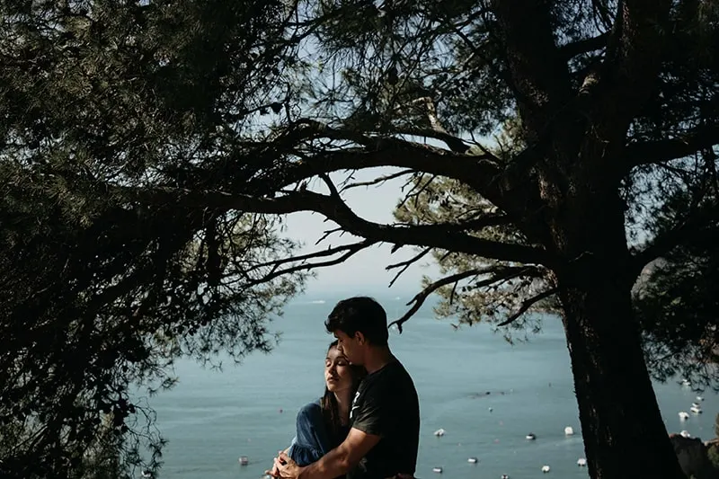 Ein Mann umarmt eine Frau, während er im Wald in der Nähe des Meeres steht