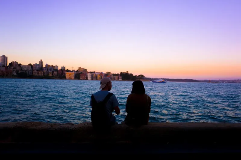 Ein Mann und eine Frau, die ein Date haben, sitzen auf dem Betonzaun und beobachten den Sonnenuntergang