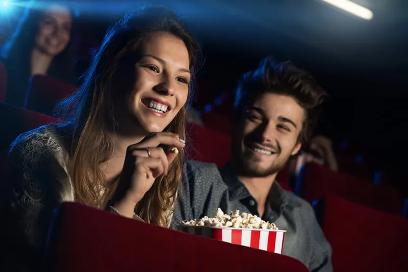 Ein Mann und eine Frau lachen im Kino, während ein Mann eine Frau ansieht