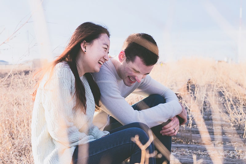 Ein Mann und eine Frau lachen zusammen, während sie tagsüber auf einer alten Eisenbahn sitzen