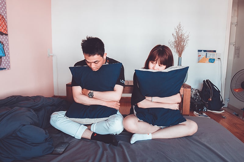Ein Mann und eine Frau sitzen auf dem Bett und umarmen die Kissen