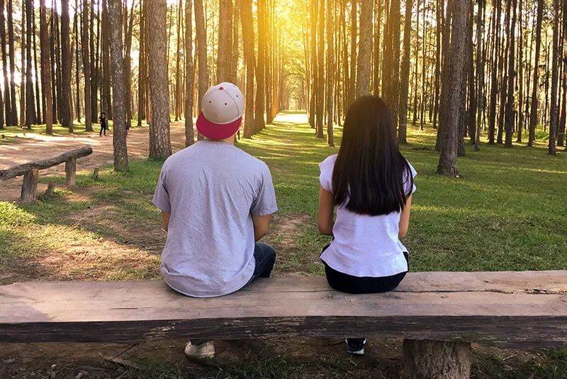 Ein Mann und eine Frau sitzen auf der Bank und zwischen ihnen stehen zwei mit Blick auf den Wald
