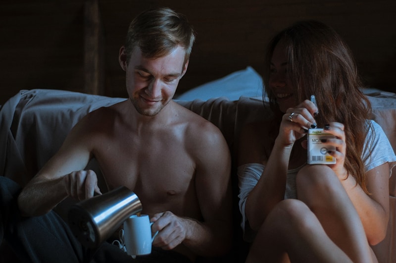 Ein Mann und eine Frau sitzen neben dem Bett, während ein Mann einen Kaffee in eine Tasse gießt