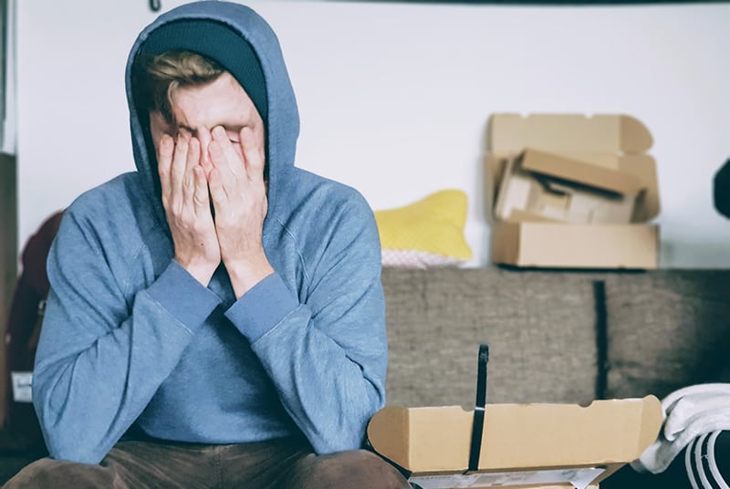 Ein Mann, der unter Druck stand und sein Gesicht mit beiden Händen bedeckte, während er auf der Couch saß