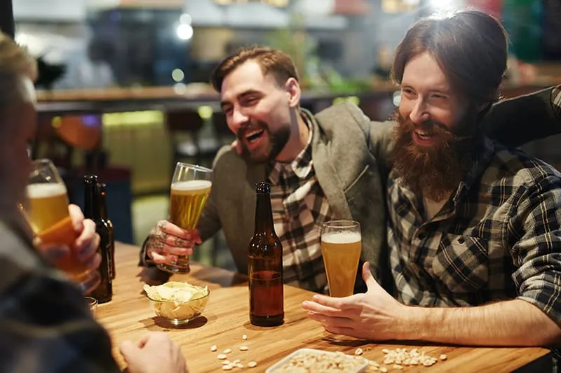 Ein betrunkener Mann umarmt seinen Freund, während er ein Glas Bier in der Bar hält