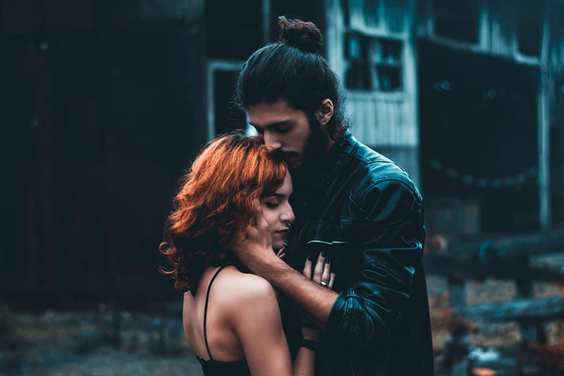 Ein dominanter Mann küsst eine Frau auf die Stirn, während er im Freien steht