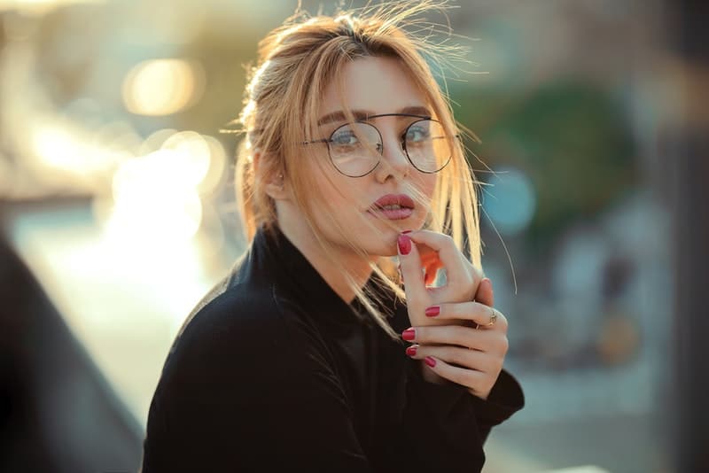 Eine Blondine mit Brille und rotem Nagellack steht nachdenklich auf der Terrasse