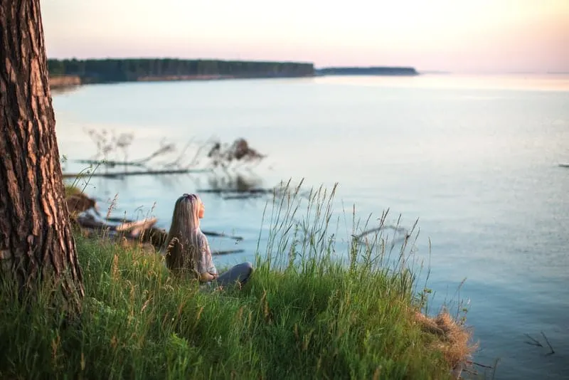 Eine Frau sitzt im Gras und schaut auf das Meer