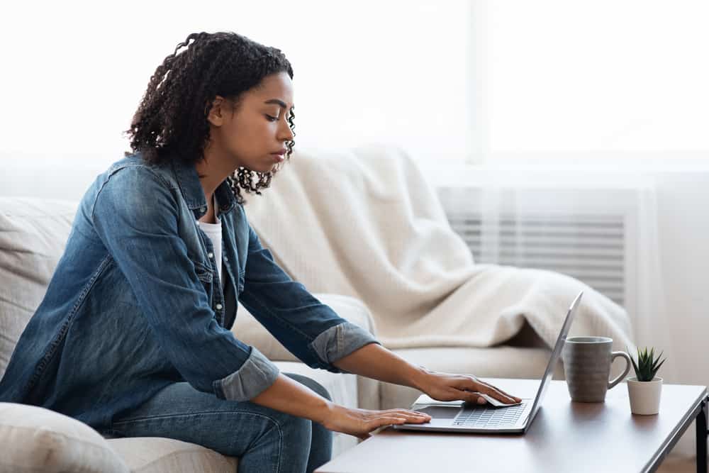 Eine schwarze Frau in einem Jeanshemd sitzt und arbeitet hinter einem Laptop