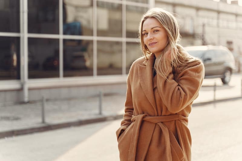Eine schöne Blondine in einem braunen Mantel geht die Straße entlang