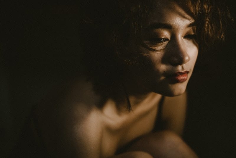 Eine traurige Frau mit brüchigem Haar sitzt zusammengerollt im Dunkeln