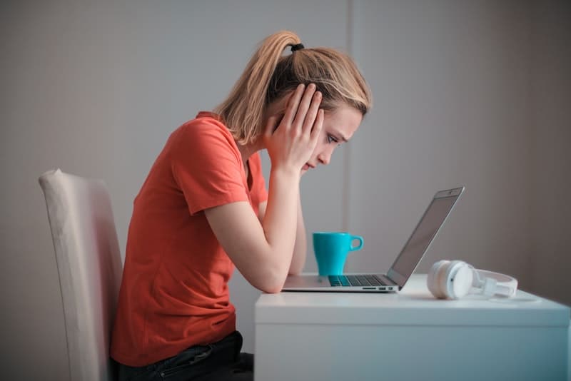 Eine unglückliche junge Frau sitzt und schaut besorgt auf etwas auf ihrem Laptop