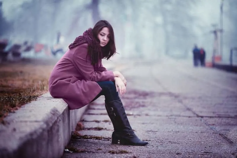 Enttäuschende junge Frau sitzt an diesem Herbsttag auf der Steinbrüstung