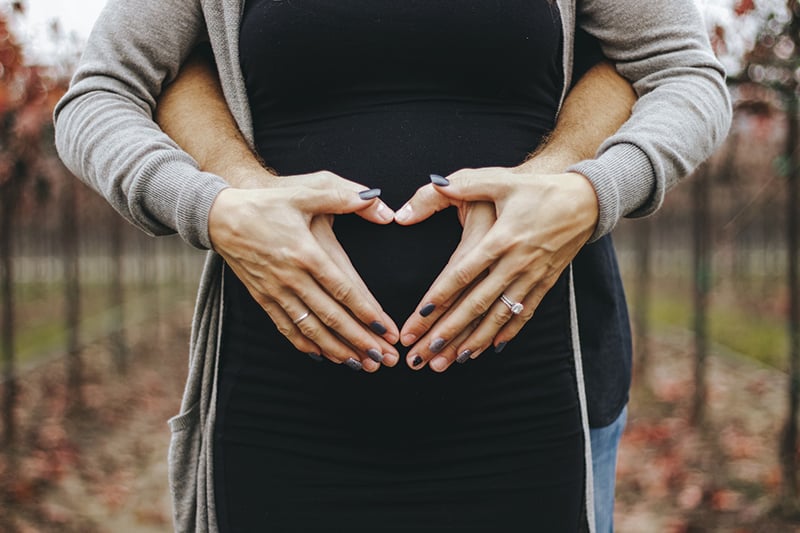 Liebespaar, das Babybauch berührt, während es eine Herzform macht mit Palmen
