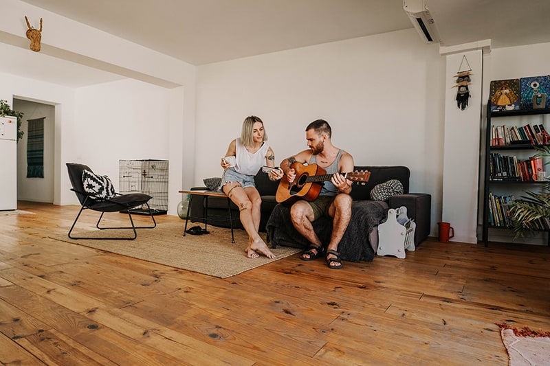 Mann, der akustische Gitarre nahe der Frau spielt, während er im Wohnzimmer sitzt
