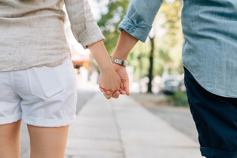 Mann und Frau, die Hände halten, während sie zusammen auf dem Bürgersteig gehen