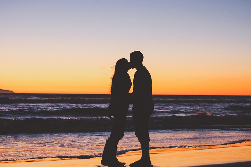 Silhouette eines Paares, das in der Nähe des Ozeans während des Sonnenuntergangs küsst