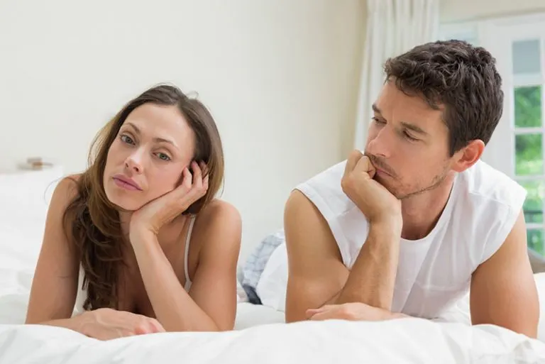 Mann, der traurige junge Frau auf dem Bett betrachtet