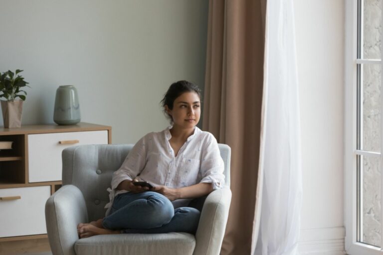 Ernste junge Frau sitzt auf dem Sofa mit Handy