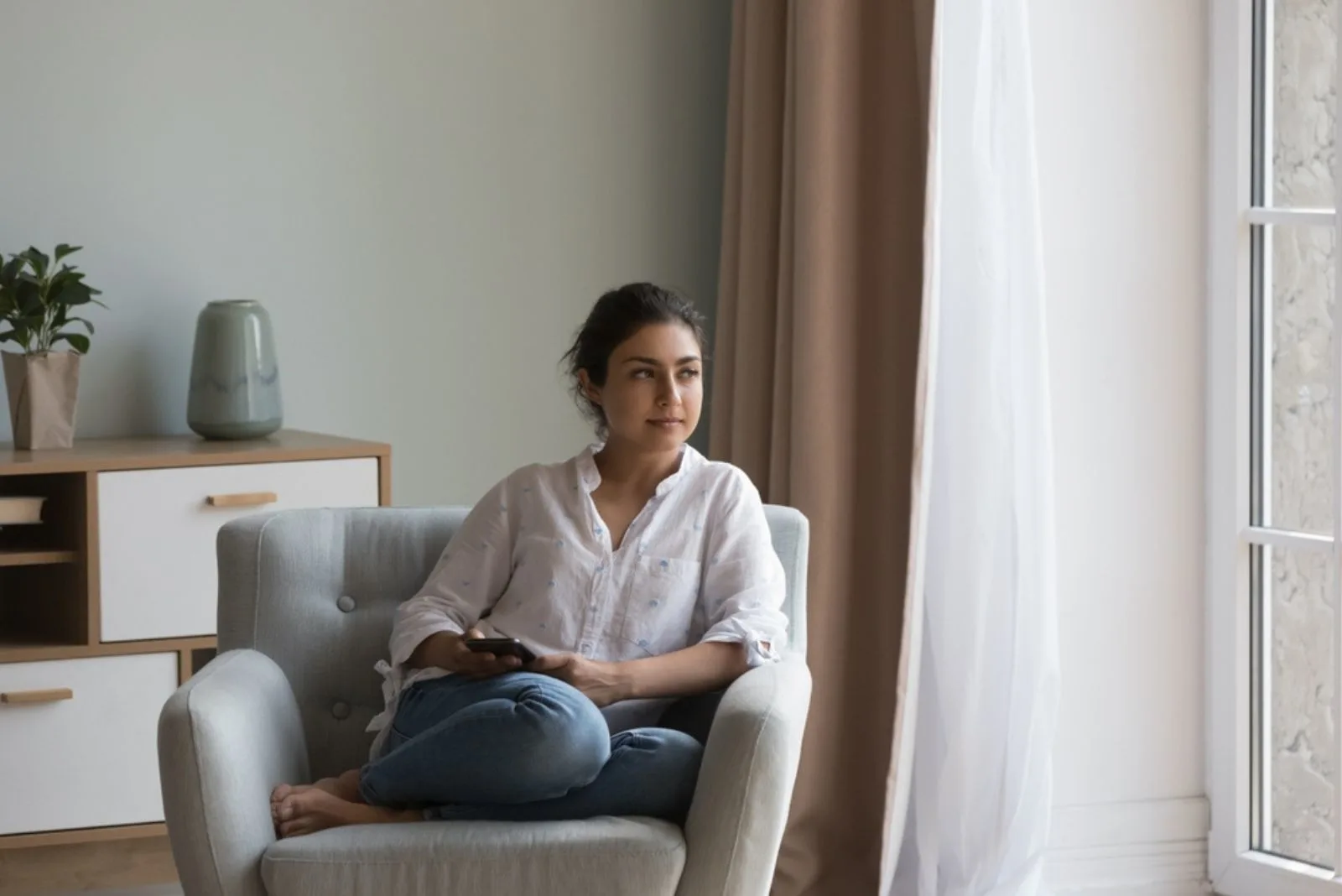 Ernste junge Frau sitzt auf dem Sofa mit Handy