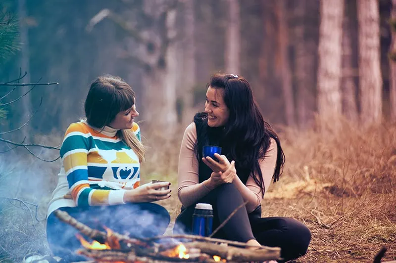 Zwei Frauen sitzen auf dem Boden im Wald in der Nähe eines Freudenfeuers