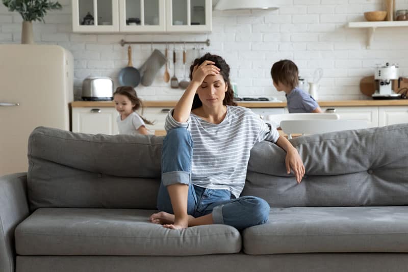 besorgte Frau, die auf der Couch sitzt, während Kinder laufen