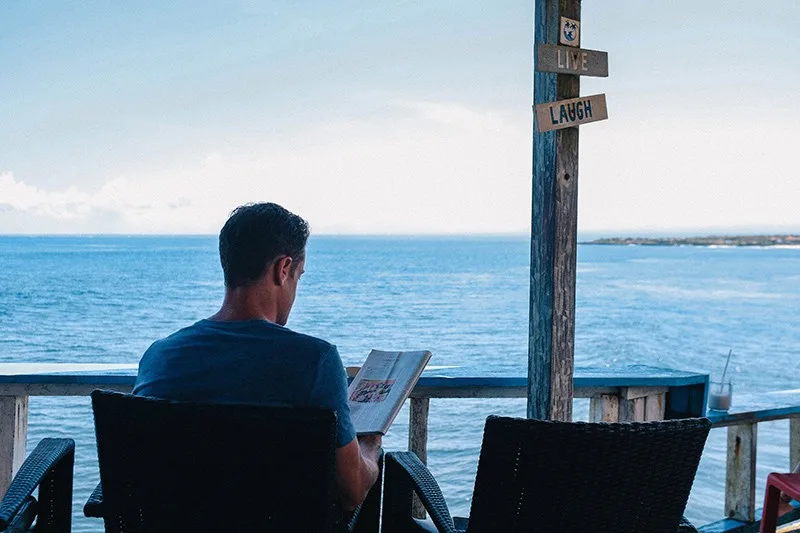 Ein Mann liest eine Zeitschrift, während er sich alleine in der Nähe des Gewässers entspannt