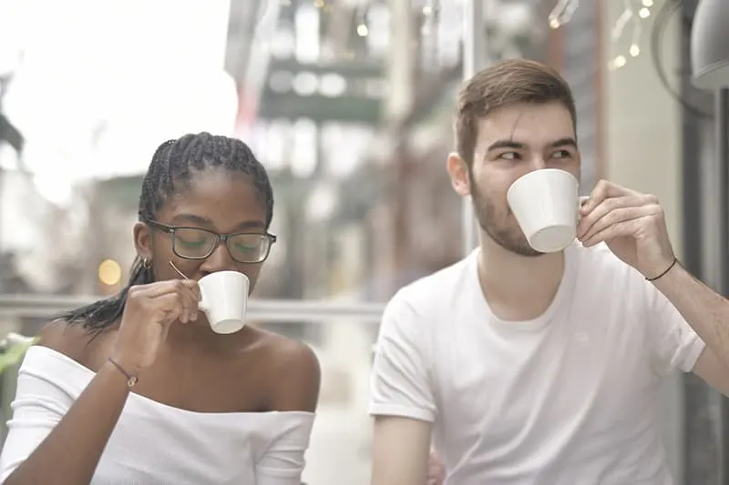 Ein Mann und eine Frau trinken gleichzeitig Kaffee, während sie zusammen im Kaffee sitzen