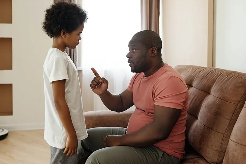 Ein Vater spricht mit seinem Sohn, während er auf der Couch sitzt und mit einem Finger zeigt