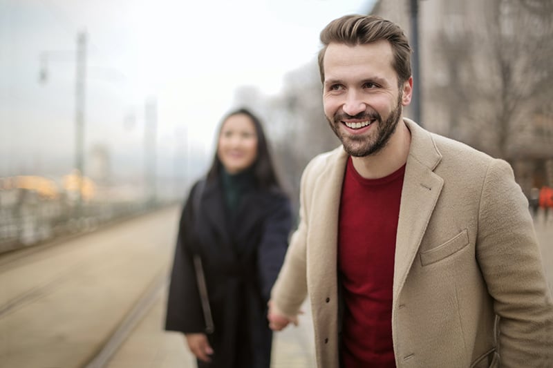 ein lächelnder Mann, der die Hand der Frau hält, während er zusammen auf dem Bürgersteig geht