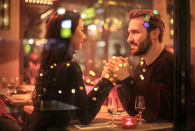 ein liebevolles Paar, das sich an den Händen hält, während es sich im Restaurant ansieht