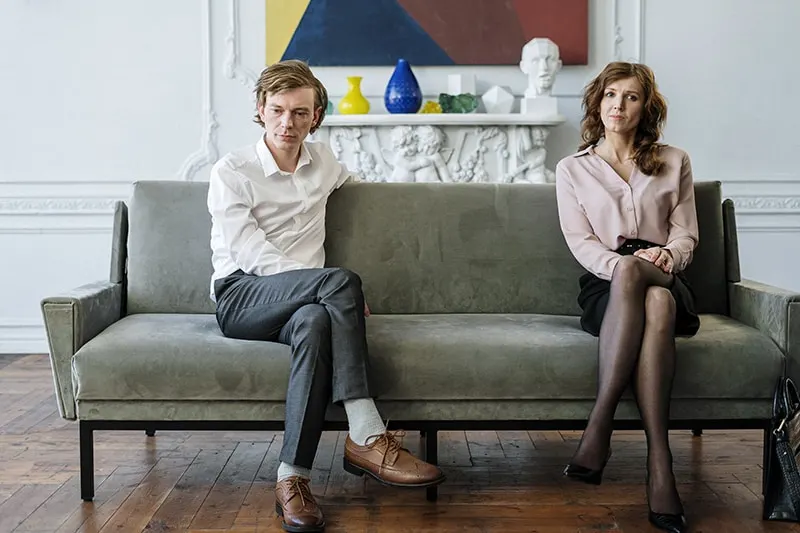 Ein nachdenklicher Mann und eine nachdenkliche Frau sitzen getrennt auf dem Sofa, während beide zur Seite schauen