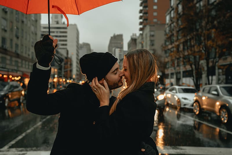 Ein Paar küsst sich im Regen, während ein Mann einen Regenschirm hält