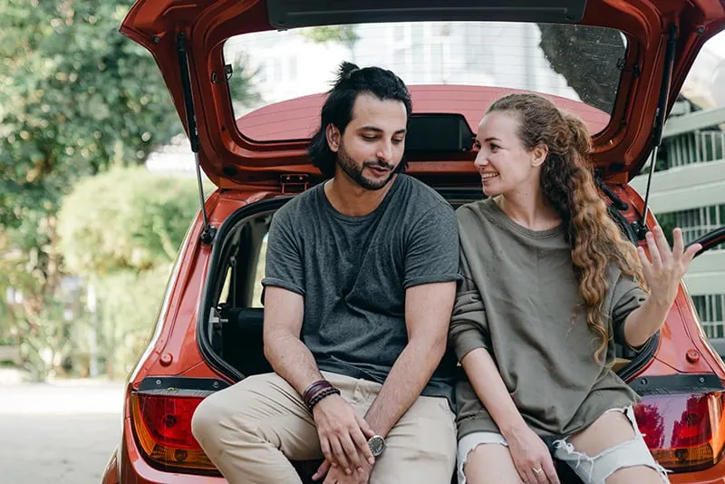 Ein Paar redet, während es zusammen auf dem Kofferraum des Autos sitzt