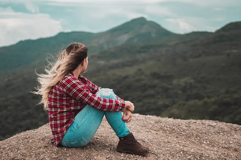 eine Frau, die alleine auf dem Boden sitzt und einen Hügel überblickt, während sie nachdenkt