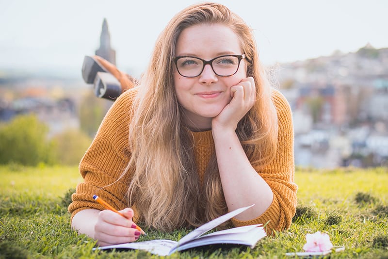 eine Frau, die auf grünem Gras liegt, während sie einen Bleistift über dem Notizbuch hält