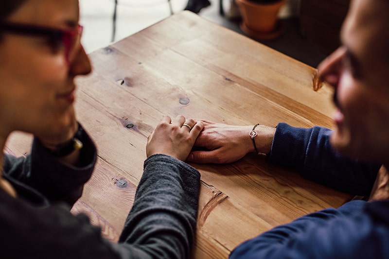 eine Frau, die die Hand eines Mannes berührt, während beide am Tisch sitzen