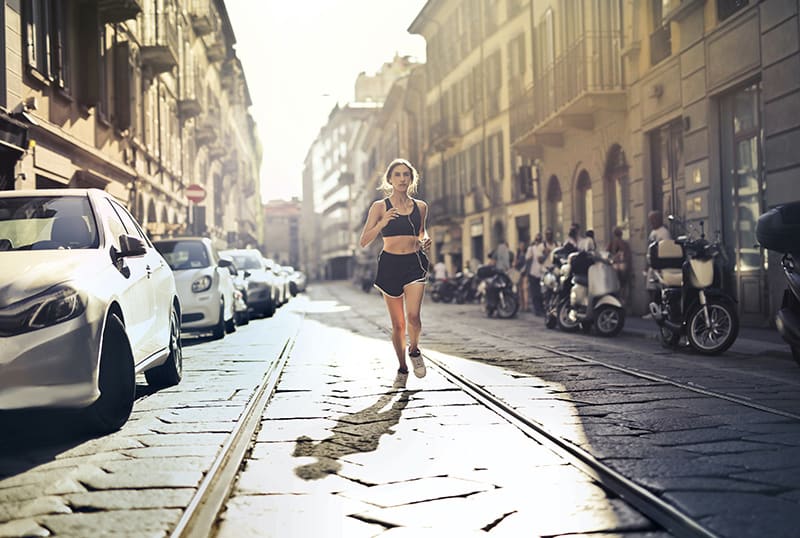 eine Frau, die die Straße entlang joggt, während sie Musik über Kopfhörer hört