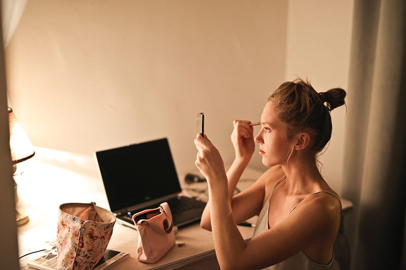 eine Frau, die Make-up aufträgt, während sie am Schreibtisch sitzt