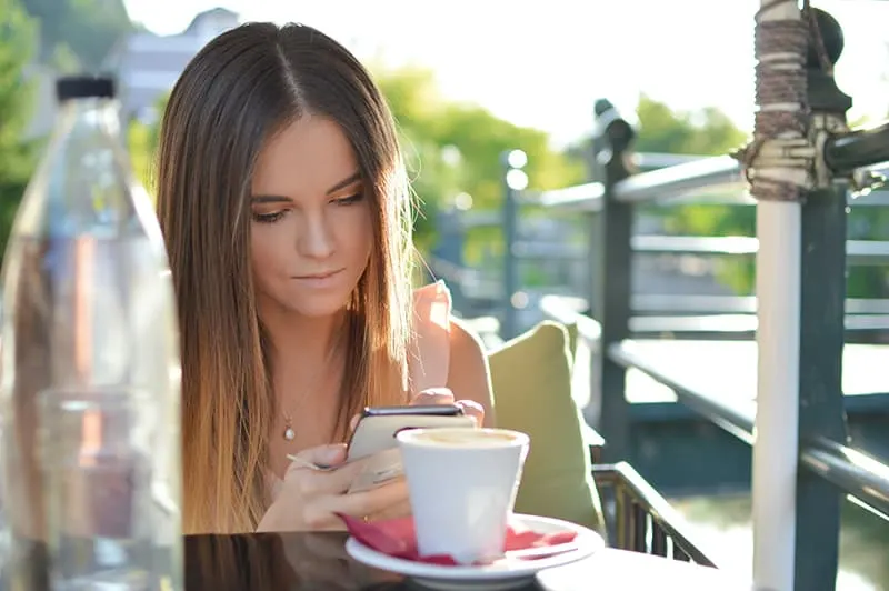 eine Frau, die eine Kontaktliste auf einem Smartphone betrachtet, während sie alleine in der Cafeteria sitzt