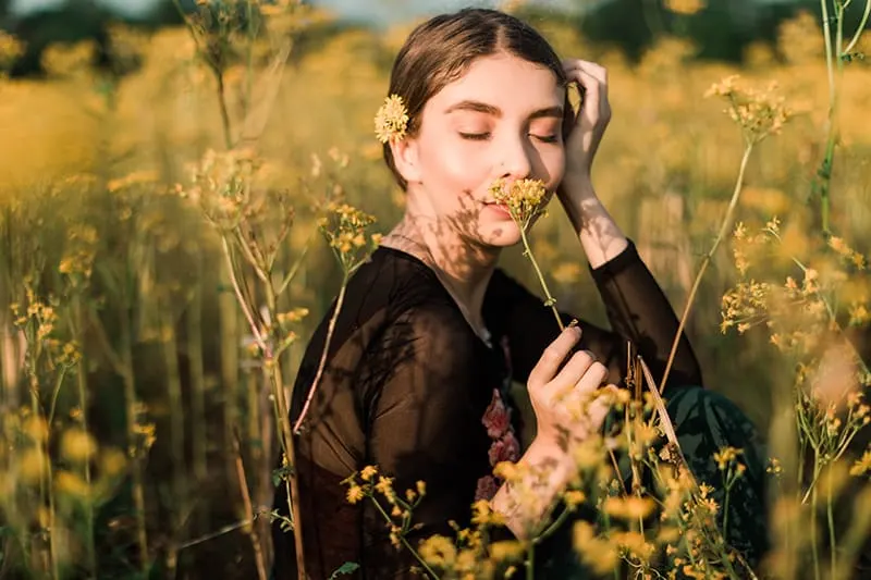 eine Frau, die eine gelbe Blume auf dem Feld riecht